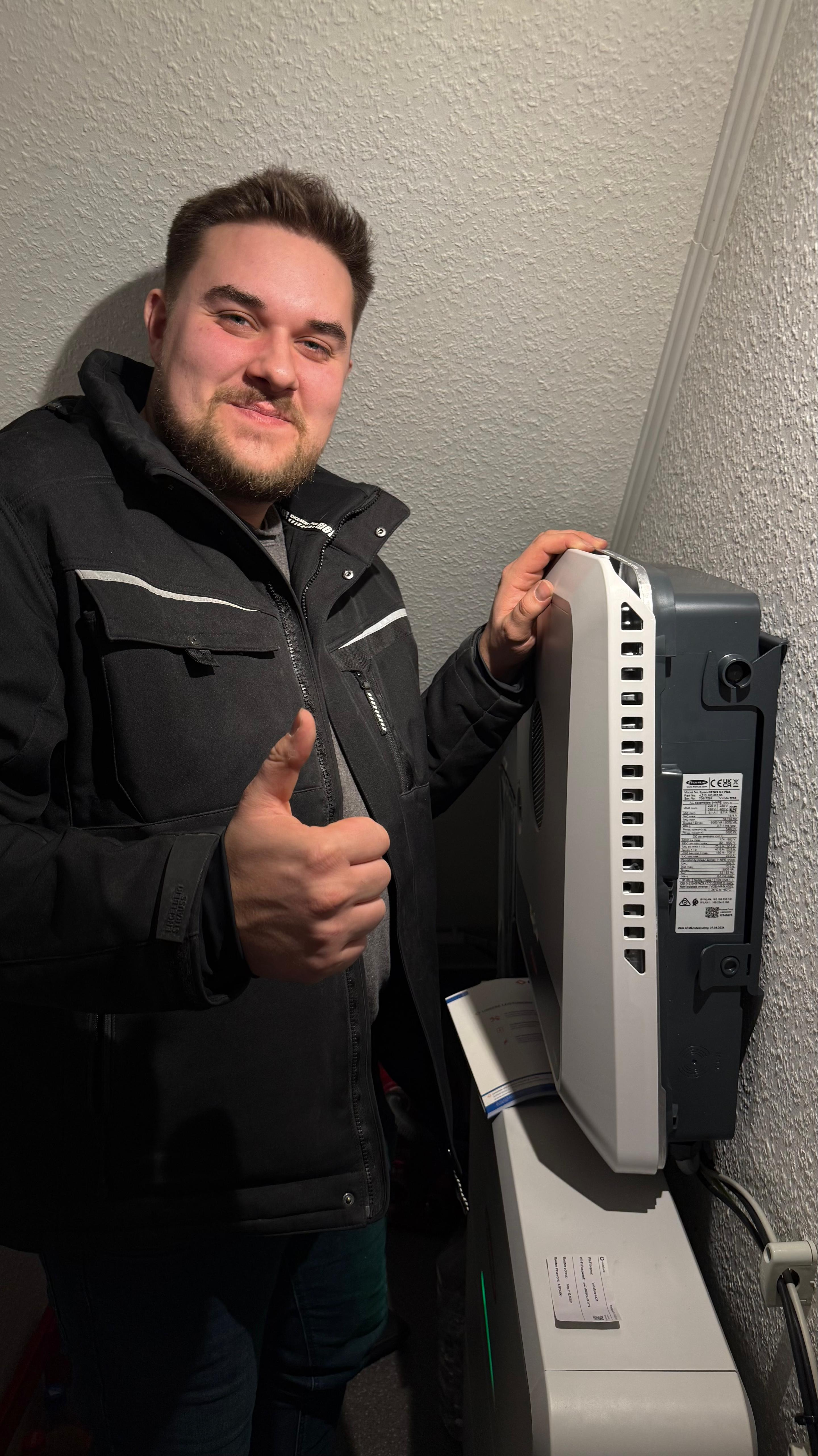 Mitarbeiter neben einer installierten W&auml;rmepumpe mit erhobenem Daumen